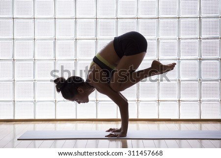Young woman practicing crow pose in a yoga studio indoors