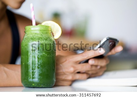 Woman holding electronic tablet while drinking a green detox juice.