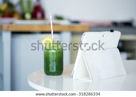 Homemade green detox juice next to a white tablet on a kitchen table