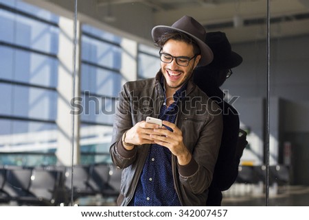 Young traveler on an airport, with a leather jacket texting with his smartphone