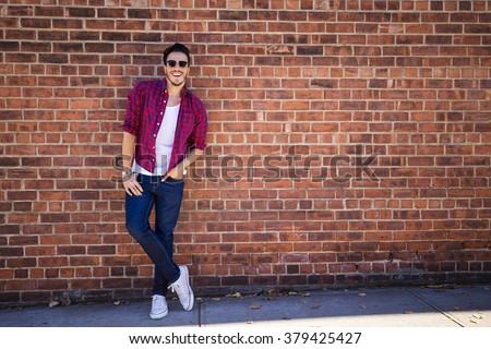 Young man wearing a check shirt and jeans against a brick wall