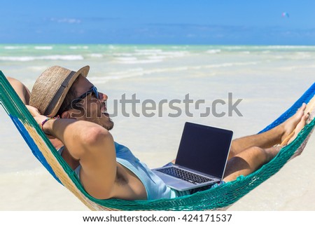 Man working with a laptop, on a hammock in the beach. Concept of digital nomad, remote worker, independent location entrepreneur.