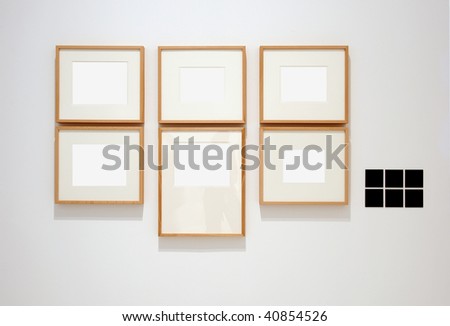 Six empty frames on white wall in museum with labels