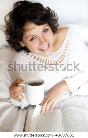 Woman reading and drinking tea on bed in sunday morning