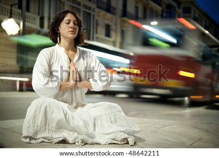 Young woman meditating in the city in a long exposure shoot with blurred traffic.