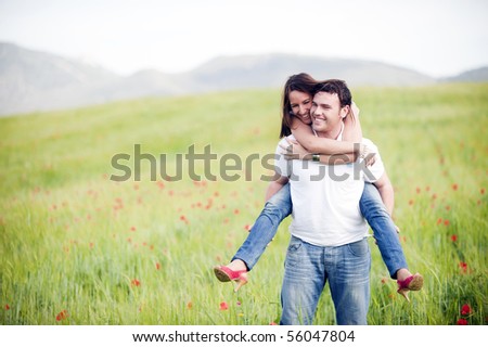 Young happy couple with her at piggiback un spring field