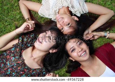 Three girl friends together lying on grass and smiling