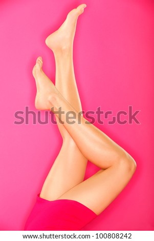 Sexy legs skin care. Woman showing beautiful female legs and bare feet on pink background.