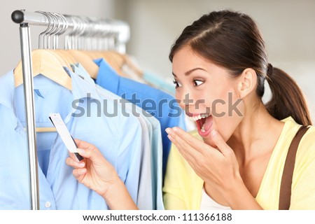 Shopper woman surprised over sale price. Happy Asian shopping woman surprised over rebate prices looking at price tag on clothes. Mixed race Asian chinese / Caucasian young female model.