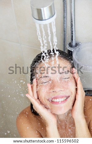 Shower woman washing face in while showering with happy smile and water splashing. Beautiful mixed race Asian Chinese / Caucasian female model home in shower cabin.