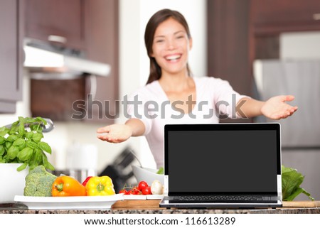 Woman showing laptop cooking in kitchen. Focus on screen with copy space. Excited mixed race asian caucasian young woman in her kitchen.