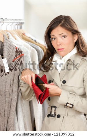 Woman shopper holding empty wallet or purse while shopping in store. Sad young woman looking at camera in clothing shop.