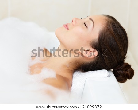 Bath woman relaxing bathing in bathtub with bath foam. Beautiful young mixed race Asian Caucasian female model in bathroom.