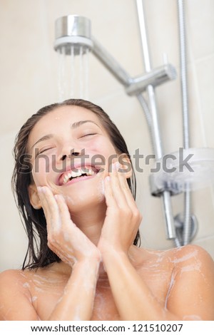 Woman washing face in shower. Showering asian woman enjoying water splashing on face while cleaning face. Portrait of multiracial Asian / Caucasian girl smiling happy. Model in her 20s.