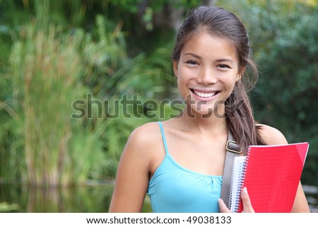 College student outside in campus park. Beautiful smiling mixed race caucasian / chinese young woman model.