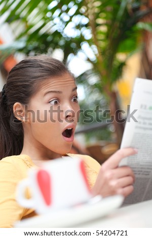Woman reading newspaper on cafe outside, shocked and surprised over the news. Young Asian woman.