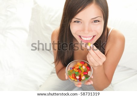 Candy woman eating sweets with a fresh smile in bed - copy space. Top view of Mixed Chinese Asian / Caucasian young female model.