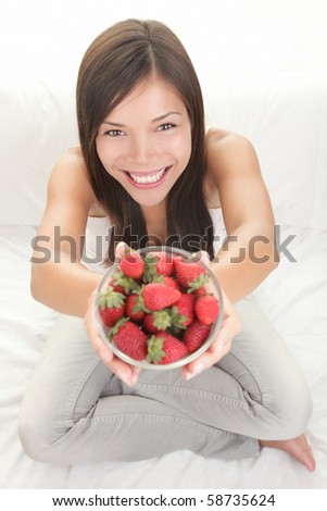 Strawberry woman showing fresh strawberries. Top view of beautiful female model sitting in bed with copy space around.