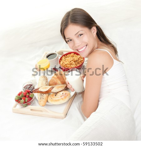 Breakfast in bed. Young woman eating breakfast in bed drinking milk. Beautiful young woman smiling.