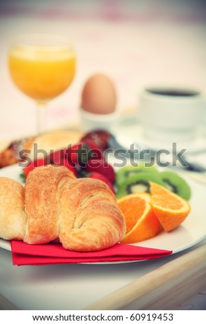 Continental breakfast. Breakfast tray on bed with coffee, orange juice, croissant, strawberries, kiwi, bread and egg. Shallow depth of field.