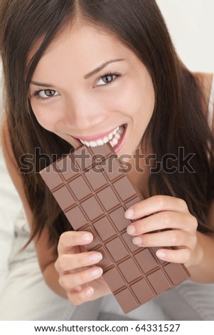 Woman eating chocolate. Beautiful happy asian girl biting a chocolate bar. Closeup isolated on white background.