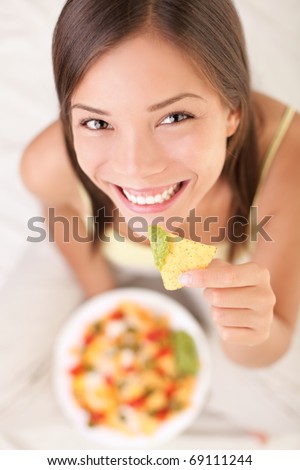Nachos eating woman smiling looking at camera. Beautiful cute girl enjoying snacks in bed - white background.