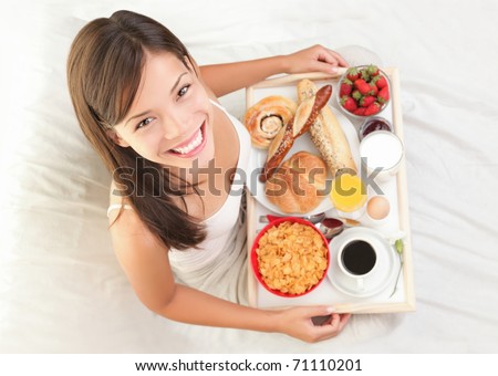 Woman having breakfast in bed. Big continental breakfast. Asian caucasian woman smiling looking at camera.