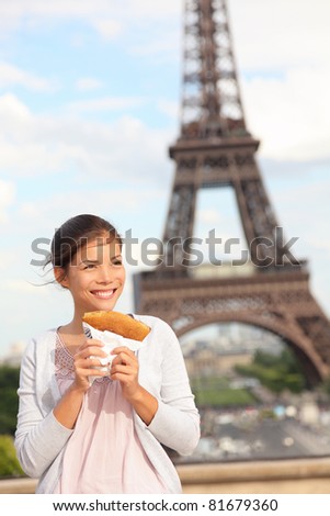 Paris woman and Eiffel Tower. Girl eating french crepe / pancake in front of Eiffel Tower, Paris, France. Mixed race Chinese Asian / Caucasian tourist.