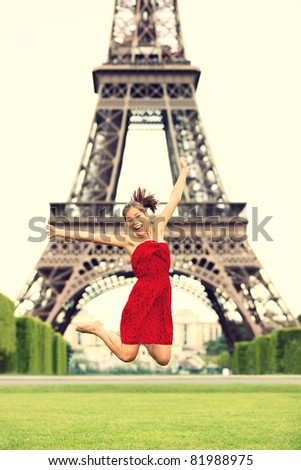 Paris girl at Eiffel Tower jumping happy smiling excited in red summer dress. Joyful young woman on Champs cheerful during vacation / holidays in Paris, France, Europe.