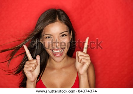 Happy energetic woman on red pointing fresh. Candid portrait of cheering beautiful young mixed race Chinese Asian / white Caucasian woman on red background.