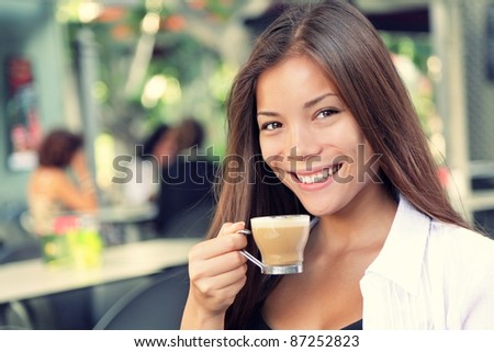 People on cafe - woman drinking coffee smiling at camera. Beautiful interracial Asian / Caucasian young woman enjoying typical spanish coffee called cortado.
