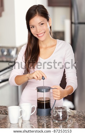 woman making coffee in kitchen - french press coffee. Mixed race Asian Caucasian female model in her twenties at home.