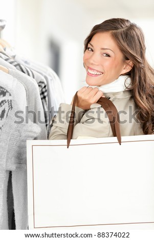Shopper woman showing shopping bag with copy space. Smiling Caucasian / Chinese Asian female model buying clothes in clothing store.