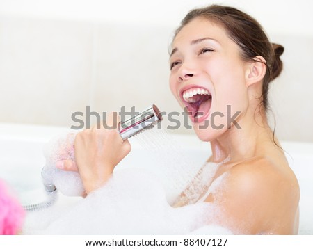Woman singing in bath with shower head. Funny image of cute Asian / Caucasian female model bathing in bathtub.