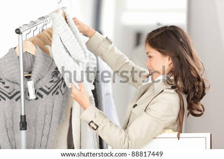 Woman shopping clothes. Shopper looking at clothing indoors in store. Beautiful happy smiling asian caucasian female model.