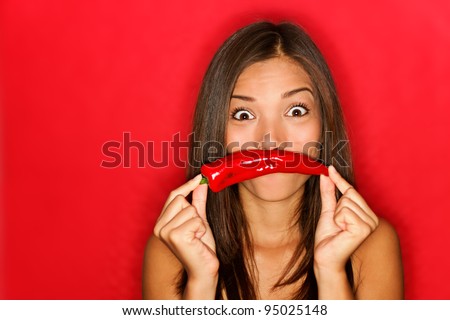 chili woman funny on red background holding red chili pepper vegetables as mustache looking funny at camera. Beautiful multicultural Caucasian / Chinese Asian girl on red background.