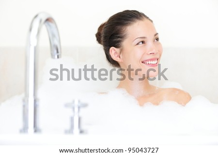 Bath woman enjoying bathtub with bath foam smiling happy. Mixed race Asian / Caucasian female model in bathroom.