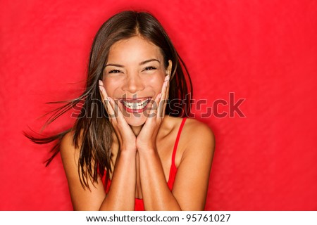 Happy girl excited. Young woman smiling very happy surprised holding head being amazed on red background. Funky young multicultural Caucasian / Chinese Asian female model joyful on red background.