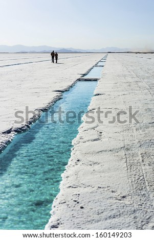 Couple walking near salt water pool on the Salinas Grandes salt flats in Jujuy province, northern Argentina.