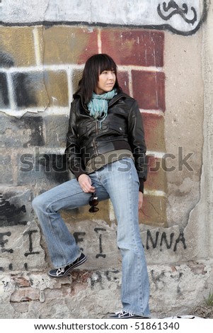 Urban Attitude. City scenery. Woman standing in dirty area.  Woman backs leaning against the wall with graffiti.