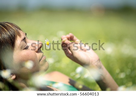 Summer. Woman on meadow smelling daisy flower.