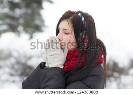 Young girl warming her frozen hands with warm breath outdoors in winter
