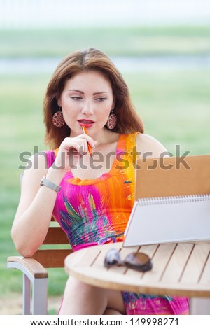 Attractive young girl doing her time management in a layback way with her leather paper notebook and fruit coctail.