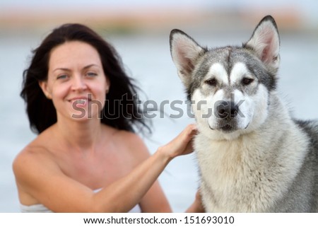 Young adult woman with her favorite pet - alaskan malamute dog on the beach in the evening