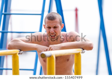 Handsome young man doing street workout on the beach in a bright summer day.