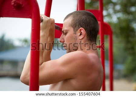 Handsome young man doing street workout on the beach in a bright summer day.
