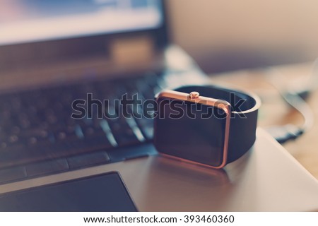 Modern smart wrist watch laying on a notebook. Trending new technology that lets you always stay connected to the internet and media. Never miss a message.Blue hipster toning