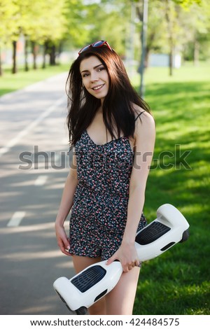 Young brunette girl riding electric mini hover board scooter in green park. Good summer weather, ecological urban transportation technology and pretty model