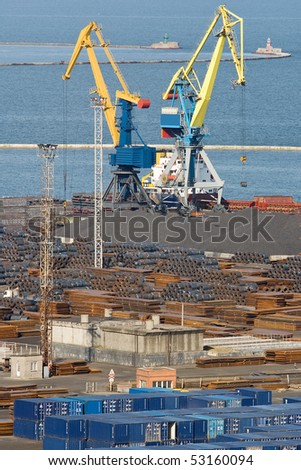 Two cranes working at the commercial docks. Container terminal and storage of metal are visible.