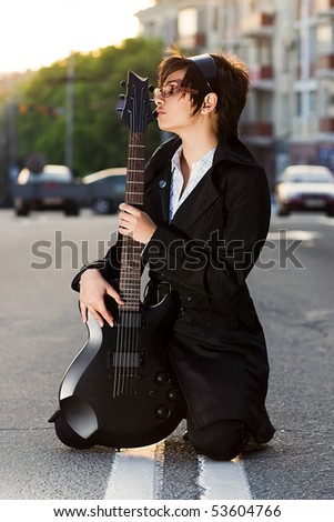 White brunette chick with black electric guitar sitting on the road